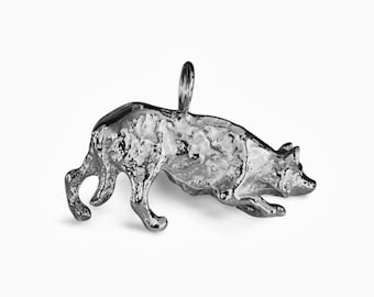 May include: A silver charm in the shape of a dog, lying down with its head turned to the side. The charm is detailed and has a textured surface.
