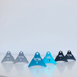 May include: A set of seven dog whistles, including two silver and five blue whistles. The whistles are triangular in shape and feature a variety of engraved designs.