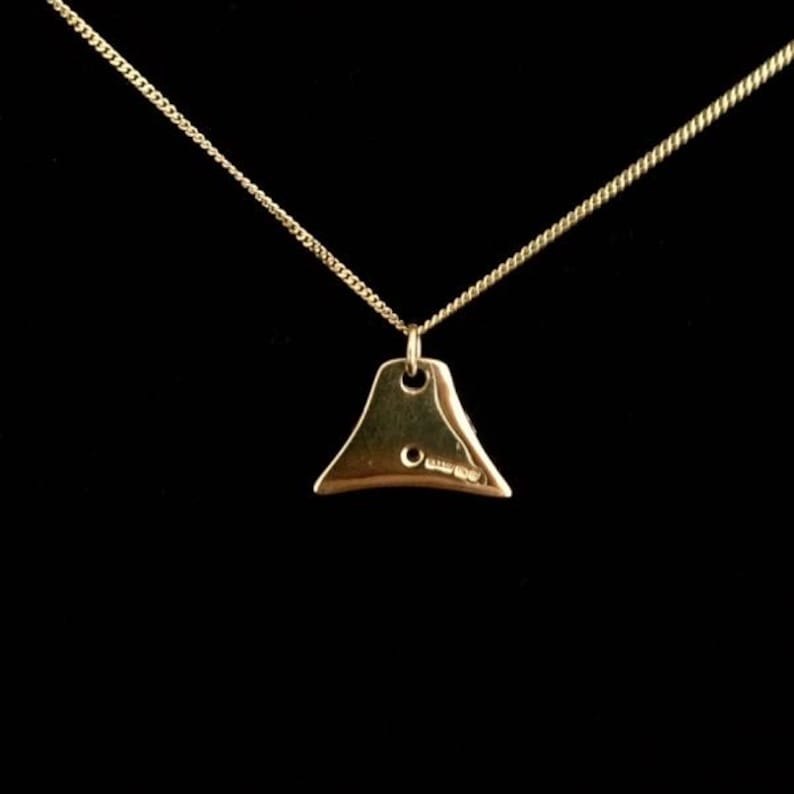 May include: A gold necklace with a small, triangular pendant. The pendant has a smooth, shiny surface and a small hole at the top for the chain to pass through.