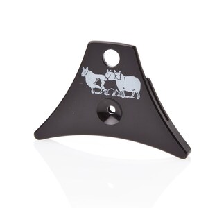 May include: Black plastic dog whistle with a triangular shape and a design of three sheep. The whistle has two holes on the top.