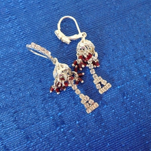 May include: A pair of silver earrings with red and clear crystal accents. The earrings are dangle style and feature a bell-shaped design.