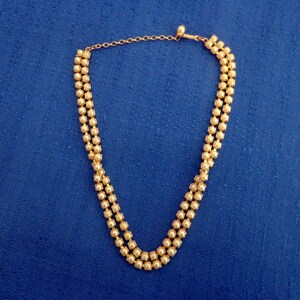May include: A gold necklace with three strands of round beads. The necklace has a clasp closure.