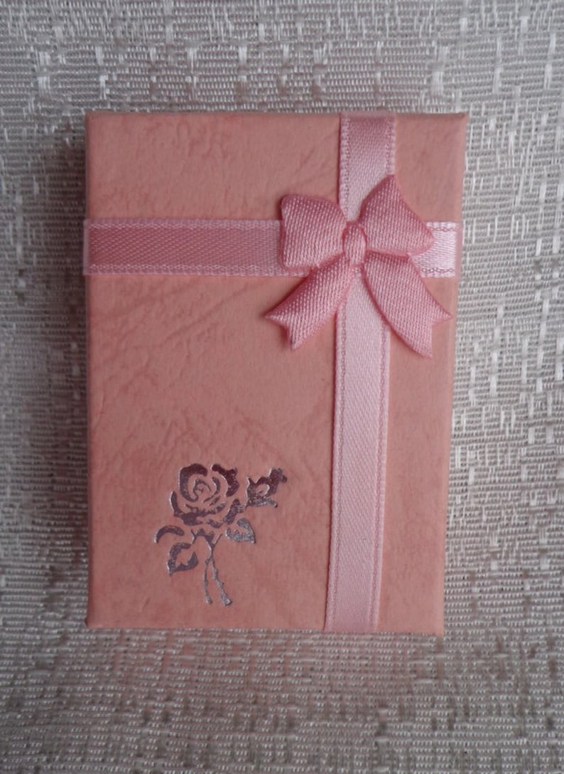 May include: A pink gift box with a satin ribbon and bow. The box has a silver embossed rose design.