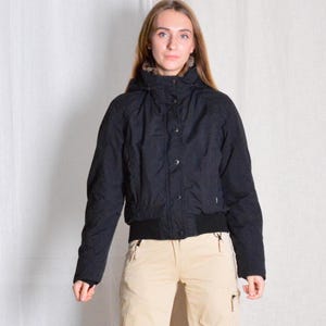 May include: A black hooded jacket with a zip and button fastening. The jacket has a ribbed waistband and cuffs. The hood is lined with faux fur.