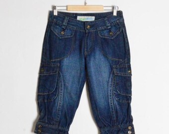 Op de afbeelding: Donkerblauwe denim capribroek met meerdere zakken en knoopdetails. De caprihangt aan een houten hanger tegen een witte achtergrond. De broek heeft een vervaagde uitstraling.