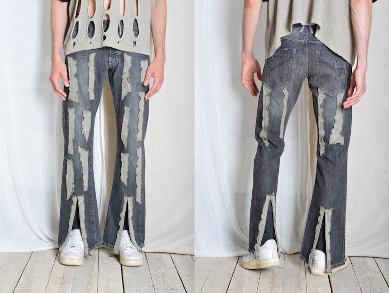 K&ouml;nnte beinhalten: Dunkelgraue Jeans mit vertikalen, hellgrauen, abgenutzten Akzenten. Die Jeans hat einen Schlitz am Beinabschluss und wird mit wei&szlig;en Turnschuhen getragen. Das Model tr&auml;gt ein hellgraues Oberteil mit Ausschnitten.
