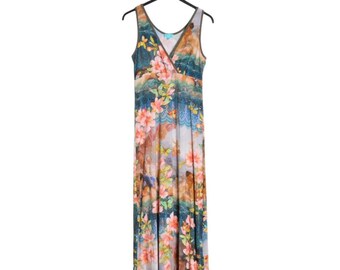 Op de afbeelding: Een mouwloze maxi-jurk met een V-hals, met een levendige bloemenprint in roze, blauwe en bruine tinten. De jurk hangt aan een zwarte hanger tegen een witte achtergrond, wat de vloeiende silhouet en het kleurrijke ontwerp benadrukt.
