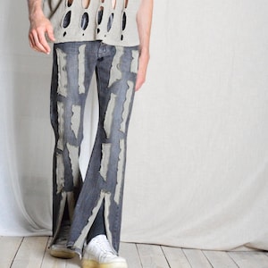K&ouml;nnte beinhalten: Dunkelblaue Jeans mit abgenutzten, hellgrauen Stoffakzenten. Die Jeans haben ein geteiltes Bein-Design und werden mit wei&szlig;en Turnschuhen kombiniert. Das Oberteil ist ein hellgraues, offen gewebtes Hemd.