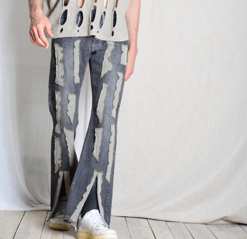K&ouml;nnte beinhalten: Dunkelblaue Jeans mit abgenutzten, hellgrauen Stoffakzenten. Die Jeans haben ein geteiltes Bein-Design und werden mit wei&szlig;en Turnschuhen kombiniert. Das Oberteil ist ein hellgraues, offen gewebtes Hemd.