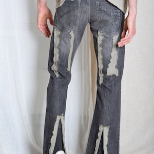 K&ouml;nnte beinhalten: Dunkelgraue Jeans mit Used-Details. Die Jeans hat vertikale, strukturierte Stoffakzente und Schlitze an den Kn&ouml;cheln. Wei&szlig;e Turnschuhe sind am unteren Ende der Jeans zu sehen.