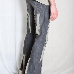 K&ouml;nnte beinhalten: Dunkelgraue Jeans mit Used-Details. Vertikale Streifen aus hellgrauem Stoff sind auf die Jeans gen&auml;ht und erzeugen ein einzigartiges Design. Die Jeans hat eine ausgestellte Bein&ouml;ffnung und wird mit wei&szlig;en Turnschuhen getragen.