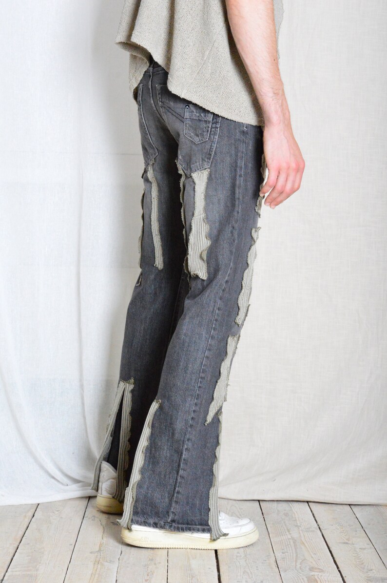 K&ouml;nnte beinhalten: Dunkelgraue Jeans mit Used-Details. Vertikale Streifen aus hellgrauem Stoff sind auf die Jeans gen&auml;ht und erzeugen ein einzigartiges Design. Die Jeans hat eine ausgestellte Bein&ouml;ffnung und wird mit wei&szlig;en Turnschuhen getragen.
