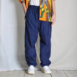 Może przedstawiać: Granatowe spodnie dresowe ze sznurkiem w pasie i elastycznymi mankietami. Spodnie wykonane są z lekkiego, wodoodpornego materiału.