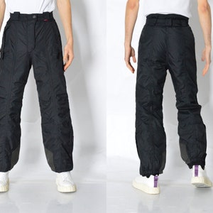 Może przedstawiać: Czarne spodnie narciarskie z zamkiem błyskawicznym i kieszeniami bocznymi. Spodnie mają sznurek w pasie i są wykonane z wodoodpornego materiału.