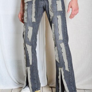 K&ouml;nnte beinhalten: Dunkelgraue Jeans mit aufgerissenen, hellgrauen Stoffflicken. Die Jeans hat einen Schlitz am Kn&ouml;chel und wird mit wei&szlig;en Turnschuhen kombiniert. Der Stil ist kantig und einzigartig.