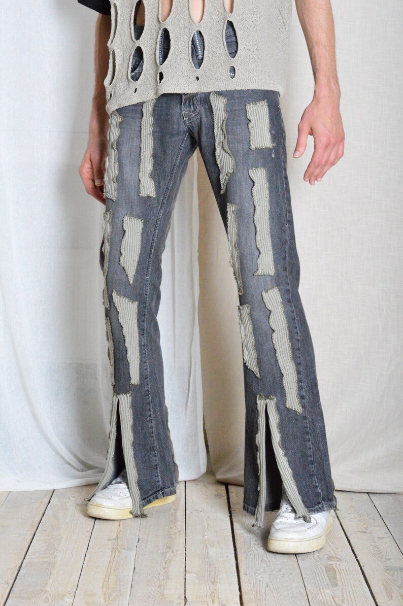 K&ouml;nnte beinhalten: Dunkelgraue Jeans mit aufgerissenen, hellgrauen Stoffflicken. Die Jeans hat einen Schlitz am Kn&ouml;chel und wird mit wei&szlig;en Turnschuhen kombiniert. Der Stil ist kantig und einzigartig.