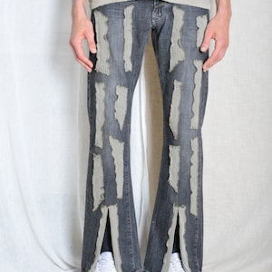 K&ouml;nnte beinhalten: Dunkelgraue Jeans mit vertikalen, strukturierten, hellgrauen Patches. Die Jeans hat ein ausgestelltes Bein-Design mit einem Schlitz am unteren Saum. Das Model tr&auml;gt wei&szlig;e Sneaker und ein hellgraues, offen gestricktes Top.