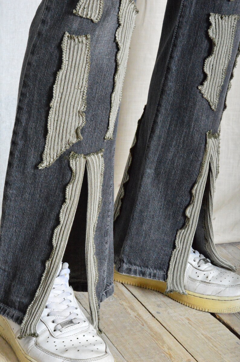 K&ouml;nnte beinhalten: Dunkelgraue Jeans mit dekorativen hellgrauen Stoffakzenten und Seitenschlitzen. Wei&szlig;e Turnschuhe sind unten zu sehen. Die Jeans haben ein einzigartiges, strukturiertes Design.