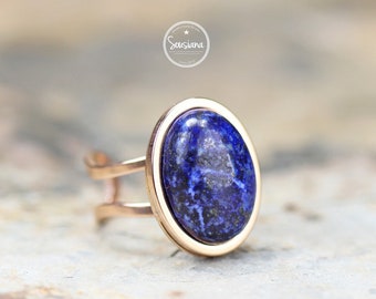 May include: A rose gold ring with a large oval lapis lazuli gemstone. The ring has a double band.