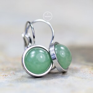 Peut inclure: Une paire de boucles d'oreilles en argent avec des cabochons de pierres pr&eacute;cieuses vertes. Les boucles d'oreilles ont un design simple et &eacute;l&eacute;gant.