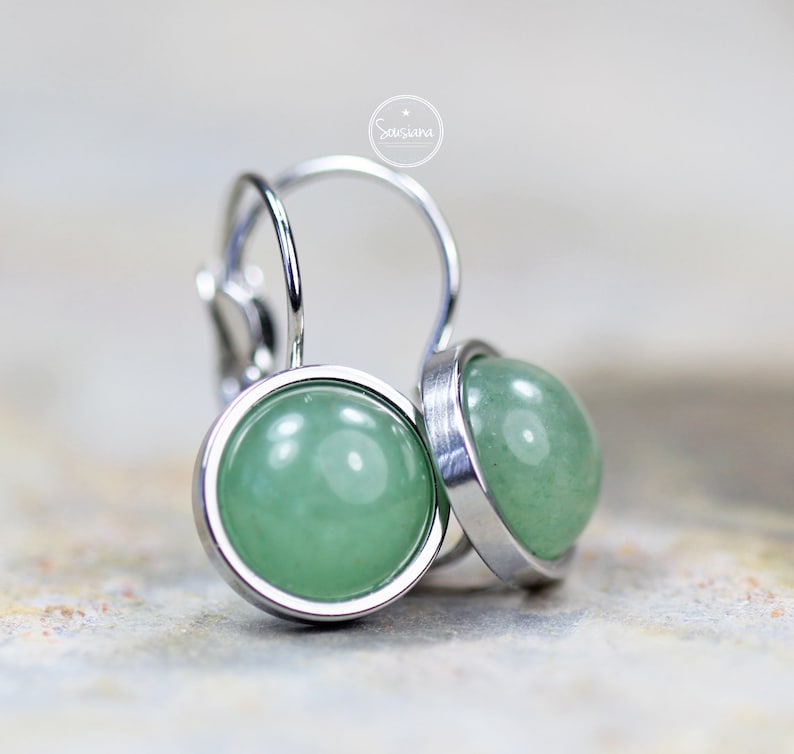 Peut inclure: Une paire de boucles d'oreilles en argent avec des cabochons de pierres pr&eacute;cieuses vertes. Les boucles d'oreilles ont un design simple et &eacute;l&eacute;gant.