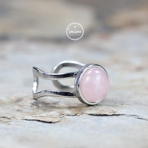 Könnte beinhalten: Ein silberner Ring mit einem rosafarbenen Rosenquarzstein. Der Ring hat ein Doppelband-Design.