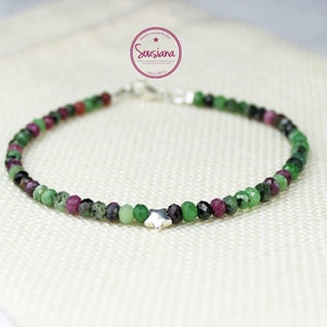 Könnte beinhalten: Ein Armband aus grünen, rosa und schwarzen Edelsteinen mit einem silbernen Sternanhänger. Das Armband besteht aus kleinen, runden Perlen und hat einen Karabinerverschluss.