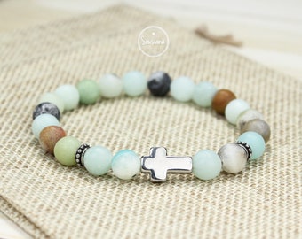 May include: A light blue and green beaded bracelet with a silver cross charm. The bracelet is made with natural stones and has a simple design.