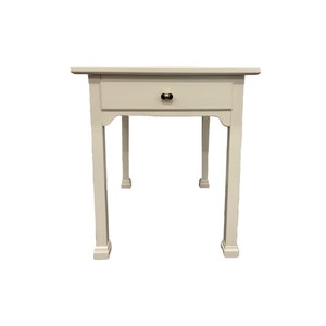 May include: White wooden table with a single drawer and four legs. The drawer has a brass knob.