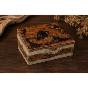 May include: A rectangular box featuring a multi-layered design with a polished top surface displaying deep brown, black, and amber marbled patterns. The sides show horizontal bands of textured beige, tan, and earthy brown mineral-like layers.