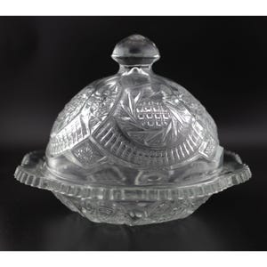 May include: A clear glass butter dish with a domed lid. The dish and lid are decorated with a cut glass pattern.