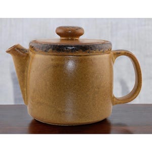 May include: A brown ceramic teapot with a lid and a handle. The teapot has a speckled glaze and a dark brown rim.