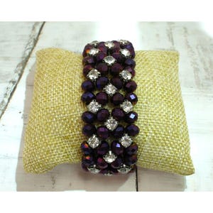 May include: A multi-strand bracelet made of dark purple faceted beads and clear rhinestones. The bracelet is elastic and has a stretchy fit.