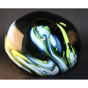 May include: A black glass paperweight with swirling patterns of green, blue, and white.