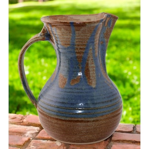 May include: A blue and brown ceramic pitcher with a wide mouth and a handle. The pitcher has a rustic, handmade look.