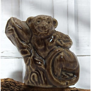 May include: A brown ceramic figurine of a monkey sitting on a tree branch. The monkey is holding a small object in its hand.