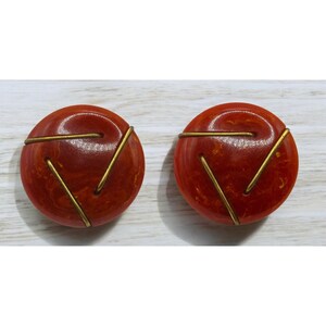May include: A pair of orange and gold earrings with a geometric design. The earrings are made of a marbled plastic with gold wire accents.