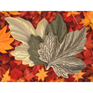 May include: Three decorative metal leaves in gold, green, and silver tones. The leaves are layered on top of each other and have a textured, realistic look.