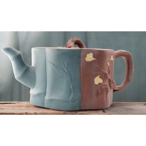May include: A blue and brown teapot with a wooden handle. The teapot has a bamboo design on one side and a floral design on the other side.