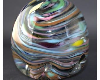 May include: A colorful glass paperweight with swirling patterns in shades of blue, green, pink, brown, and yellow. The paperweight has a rounded shape and a smooth, glossy finish.