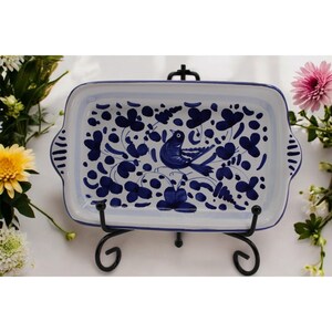 May include: Rectangular white ceramic serving dish with a blue bird and floral design. The dish is supported by a black metal stand and has handles on each side. The design features a bird and floral pattern in shades of blue.