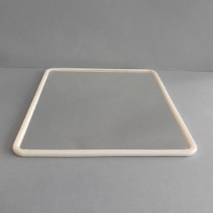 May include: A clear, rectangular glass pane with a rounded, off-white frame. The frame is a continuous, smooth line that outlines the glass. The image is set against a solid gray background, highlighting the simplicity of the design.