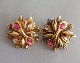 May include: A pair of gold-tone metal earrings featuring a starburst design with textured, radiating petals. Each earring is accented with two teardrop-shaped fuchsia pink crystals and two clear, marquise-cut crystals set in the center.