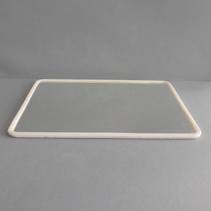 May include: A rectangular mirror with a rounded, off-white frame. The mirror is set against a gray backdrop, creating a clean and minimalist aesthetic. The frame's smooth lines and neutral color suggest a modern design.