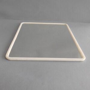 May include: A square, frameless mirror with a thick, off-white border. The mirror is rectangular with rounded corners and is set against a gray background. The border is smooth and uniform in width.