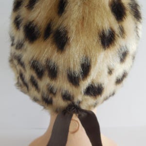 May include: A vintage-style hat with a faux fur leopard print design. The hat features a beige base with dark brown spots and a brown ribbon tie at the back. This accessory is a stylish addition to any wardrobe.