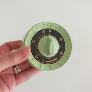 Peut inclure: Un minuteur de cuisine vert menthe vintage avec un cadran noir et des chiffres blancs. Le minuteur a un bouton central et un design circulaire avec le texte "GOUPATAN" et "ARMER A FOND ET REVENIR SUR LE TEMPS CHOISI".