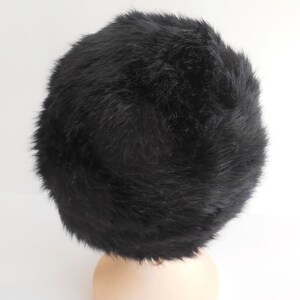May include: A black, fluffy hat with a rounded shape. The hat is made of a soft, fur-like material. The hat is shown from a top-down perspective.