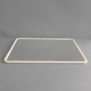 May include: A rectangular mirror with a rounded, off-white frame. The mirror's reflective surface is smooth and clear, set against a neutral gray background. The frame's corners are gently curved, creating a soft, modern aesthetic. The mirror is a decorative item.
