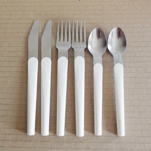 Peut inclure: Un ensemble de six couverts comprenant deux couteaux, deux fourchettes et deux cuillères. Chaque ustensile est composé d'une tête en métal argenté et d'un manche blanc uni. Les objets sont disposés en rangée verticale sur une surface plane.